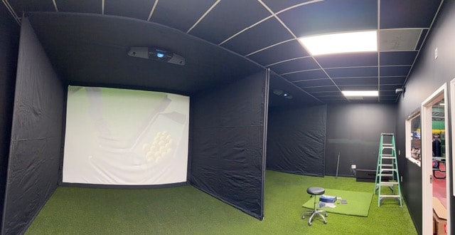 Indoor golf simulator room with turf flooring and projection screens