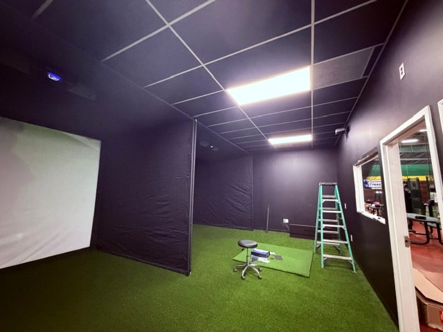 Golf simulator bay with black painted walls and turf installation